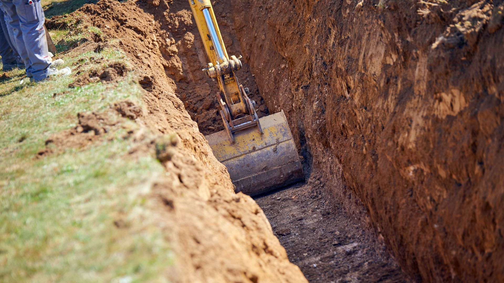 Excavator digging a deep trench in dirt with grassy ground nearby