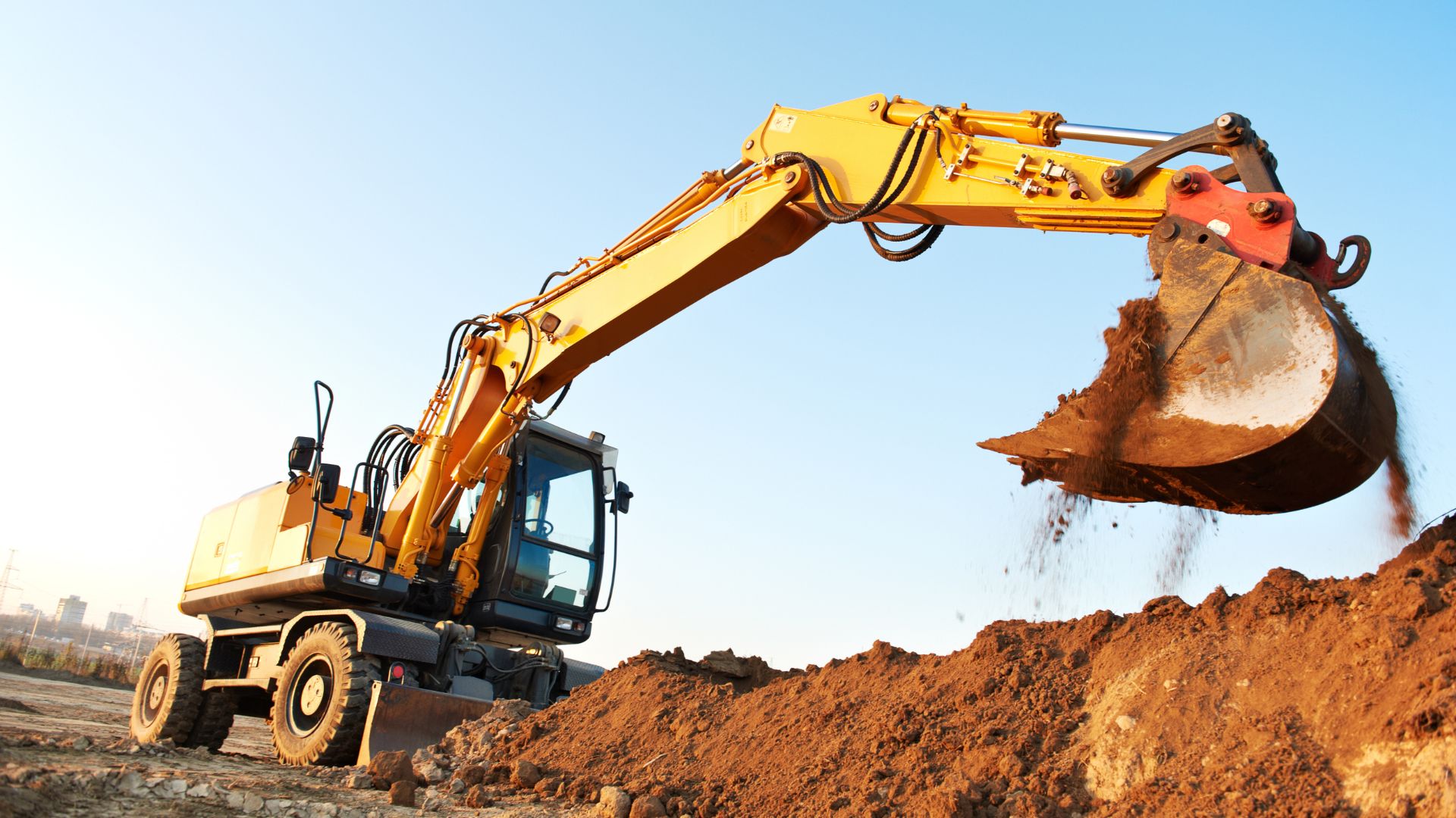 Yellow wheeled excavator digging and moving dirt at construction site