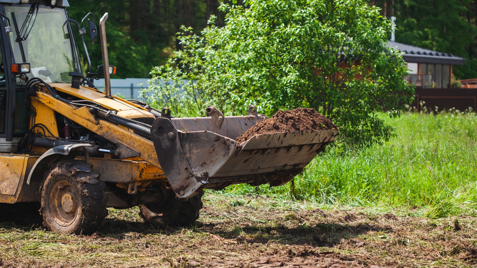 Yellow backhoe loader scooping dirt in grassy outdoor construction area